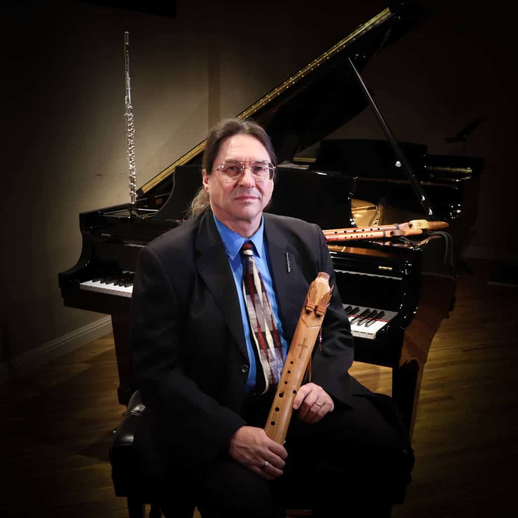 Jim seated at piano holding Native American flute